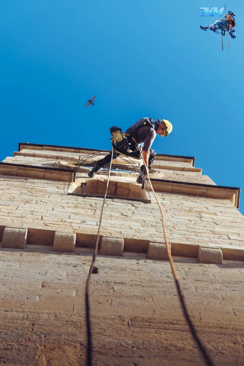Technicien cordiste descendant en rappel le long de la tour du clocher de l'abbatiale romane de Saint-Gilles-du-Gard