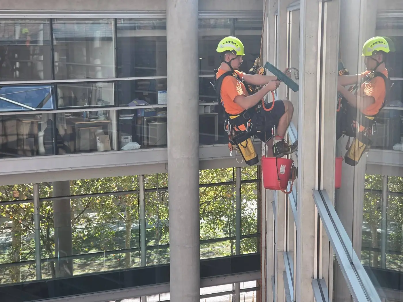 Cordiste 2KM qui lave une vitre du hall du palais de justice de Toulouse au mouilleur, son reflet dans le vitrage