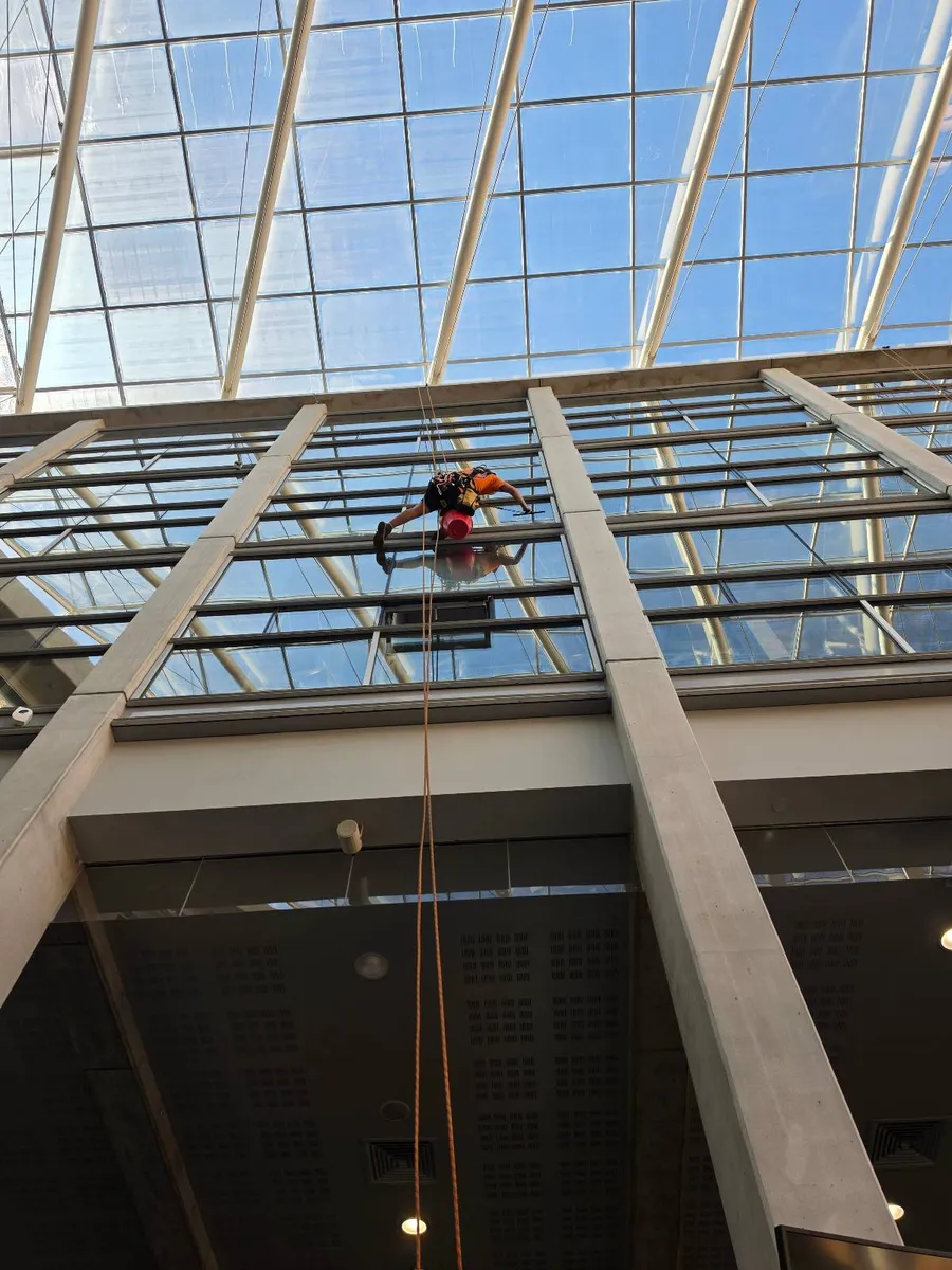Cordiste suspendu sous la verrière de l'atrium du Tribunal judiciaire de Toulouse, vu depuis le bas