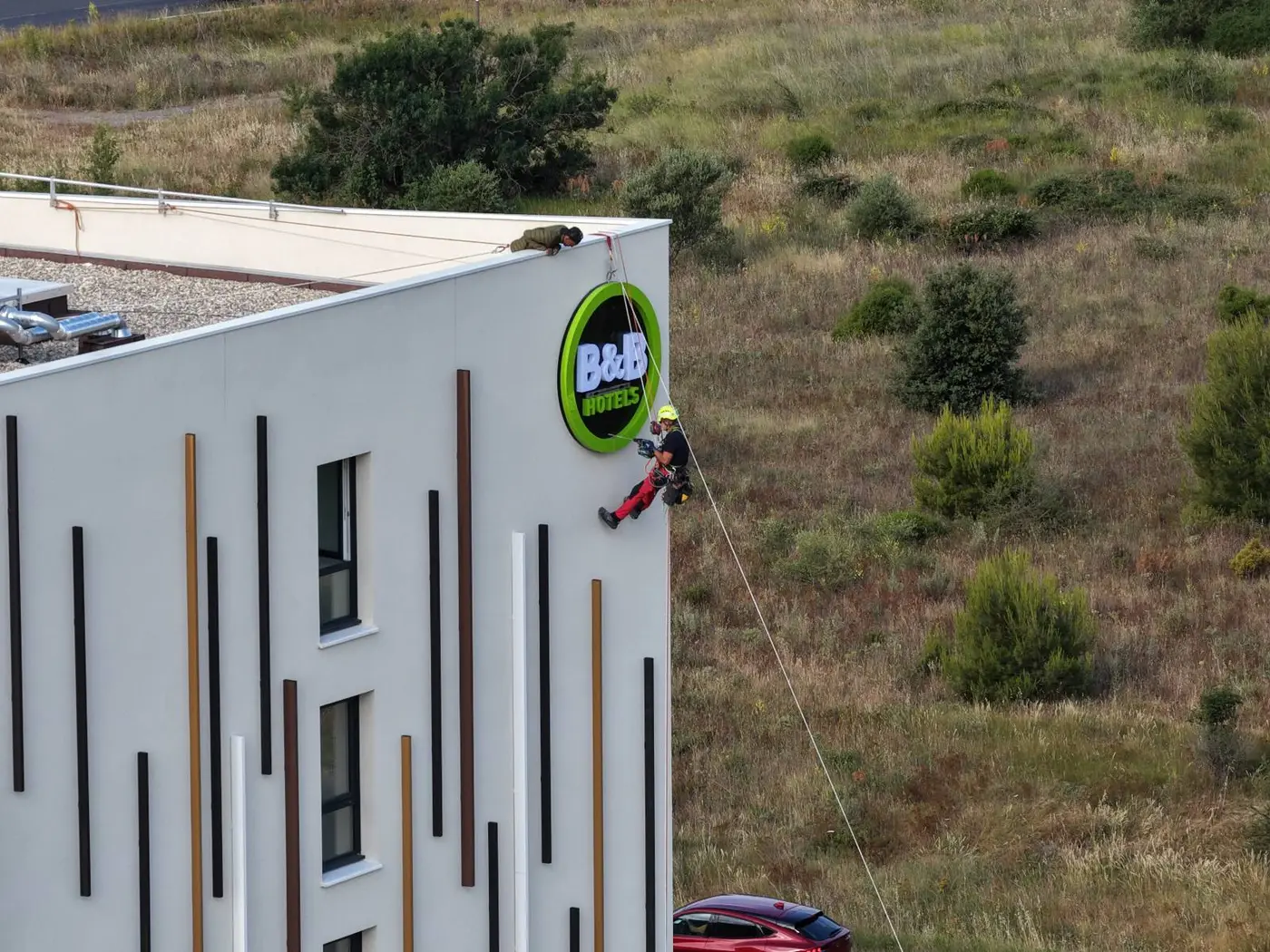 Cordiste réalisant le perçage de fixation à plus de 25 m de hauteur sur la façade de l'hôtel B&B Bessan