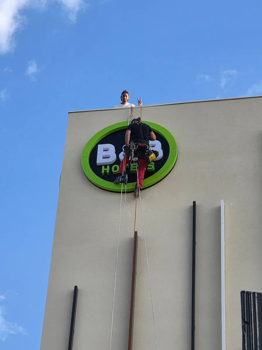 Technicien cordiste positionnant une enseigne B&B sur la façade du nouvel hôtel de Bessan