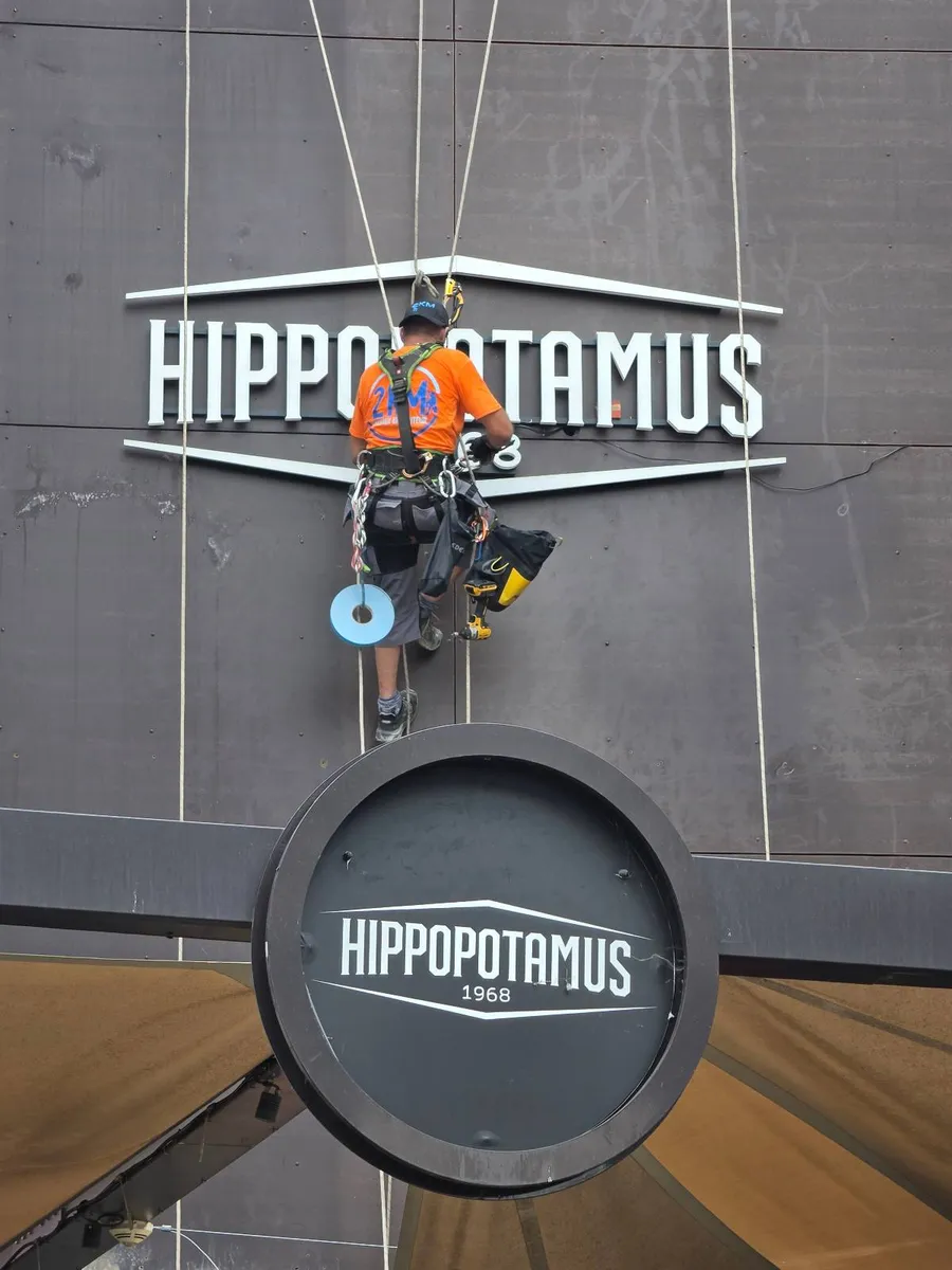 Technicien cordiste 2KM réalisant les raccordements électriques de l'enseigne HIPPOPOTAMUS en façade