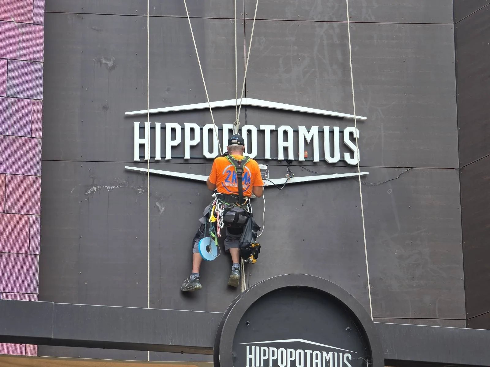 Pose de l'enseigne au-dessus de l'entrée du restaurant Hippopotamus et branchement du câble électrique